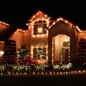 red holiday lights framing residential homes roof bushes archway white holiday lights wrapping trees bushes